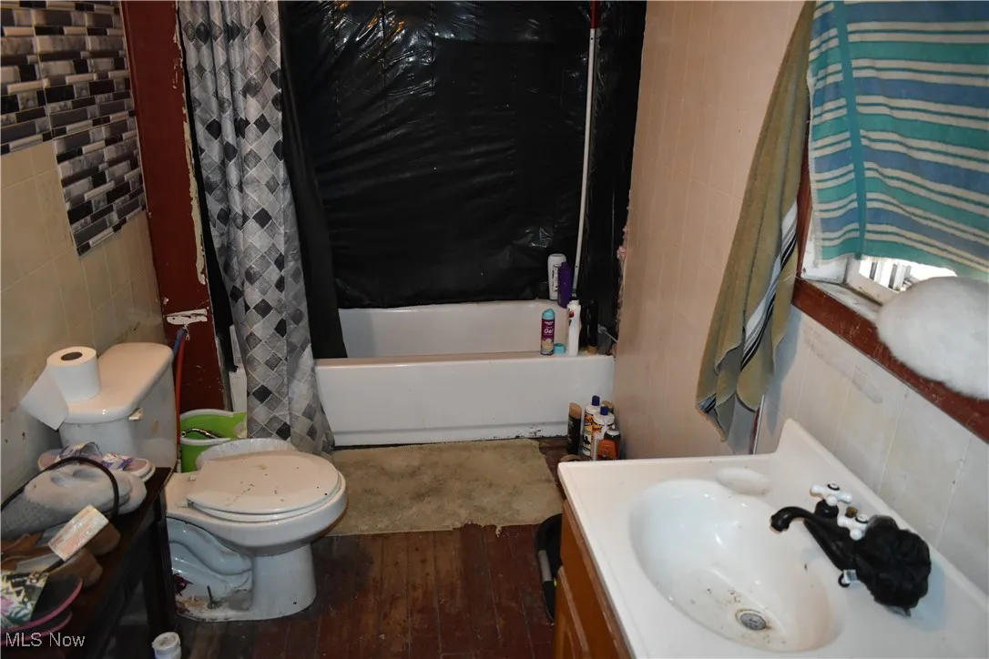 Bathroom with vanity, wood finished floors, shower / bath combo, tile walls, and toilet