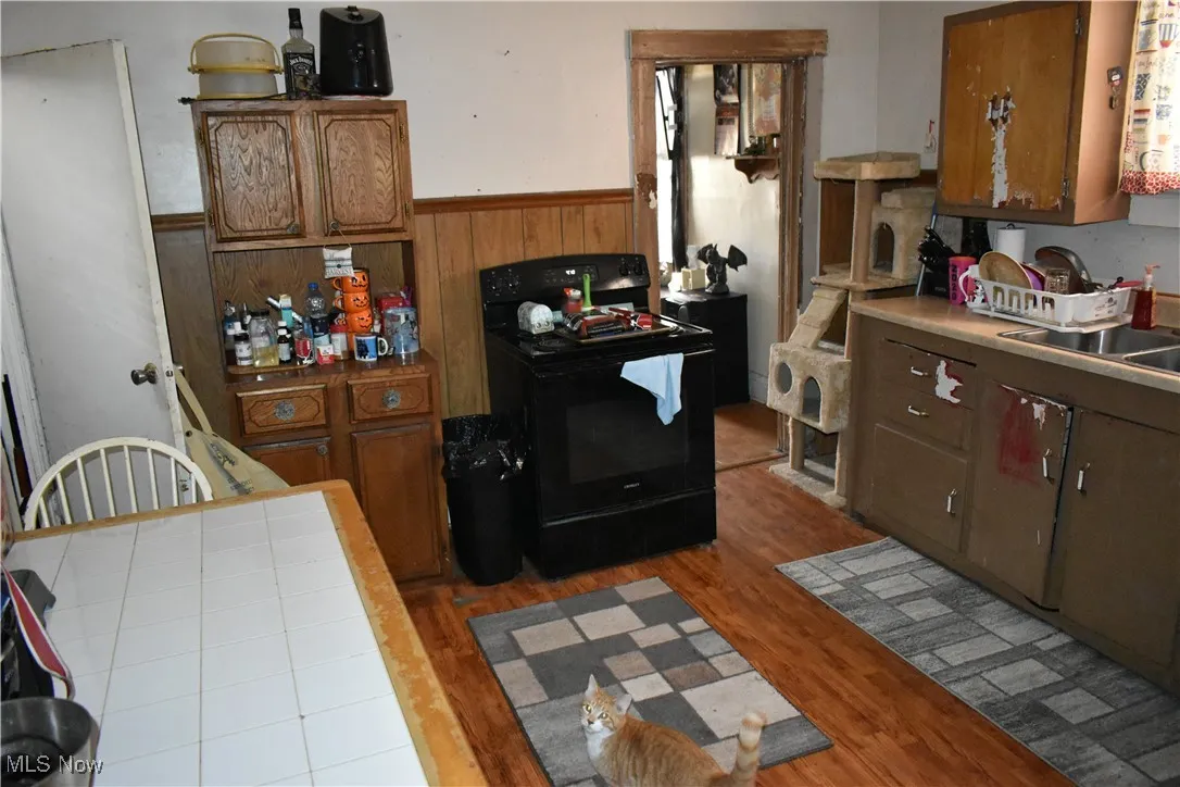 Kitchen featuring a wainscoted wall, brown cabinets, light wood-style flooring, and black electric range oven