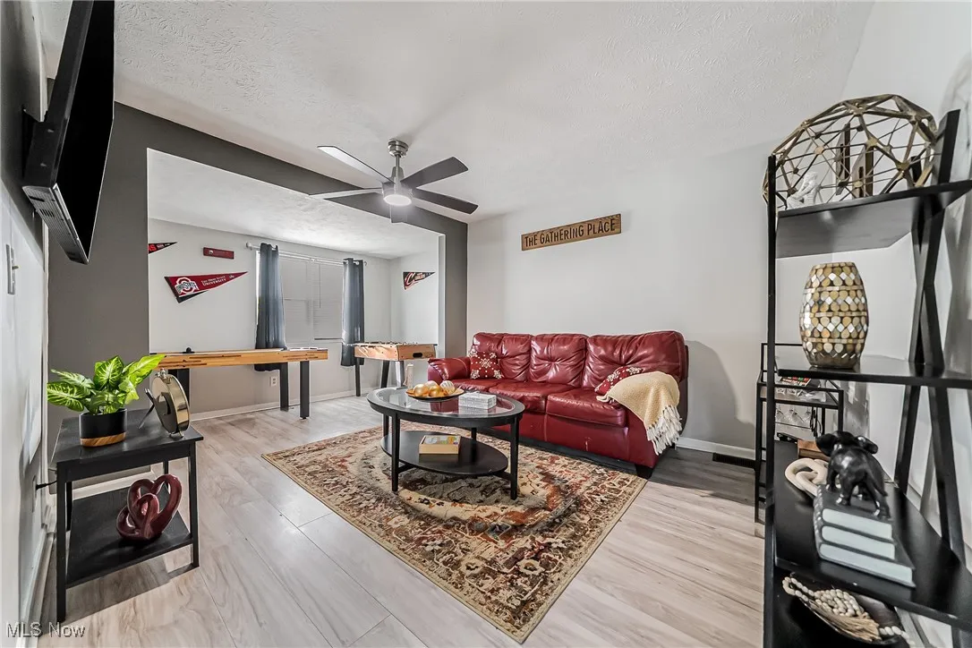 Living area featuring ceiling fan, a textured ceiling, baseboards, and wood finished floors