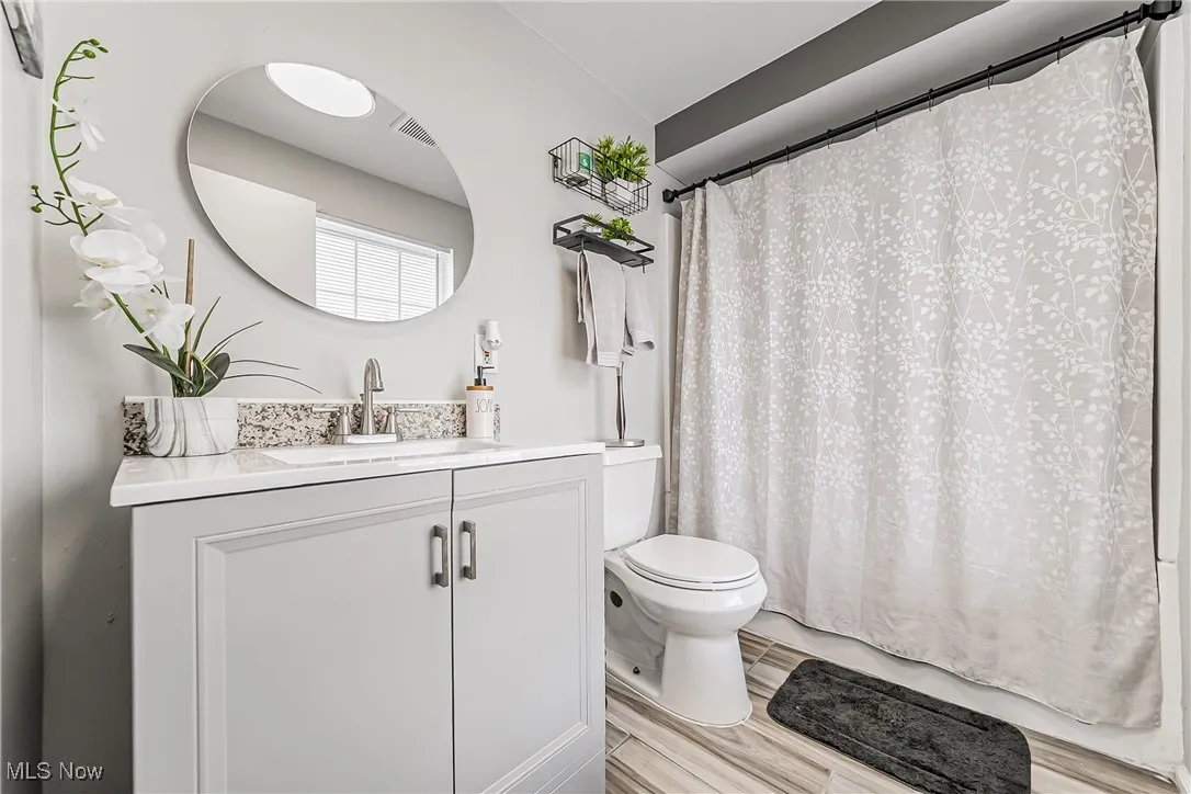 Full bath featuring a shower with curtain, visible vents, vanity, and toilet