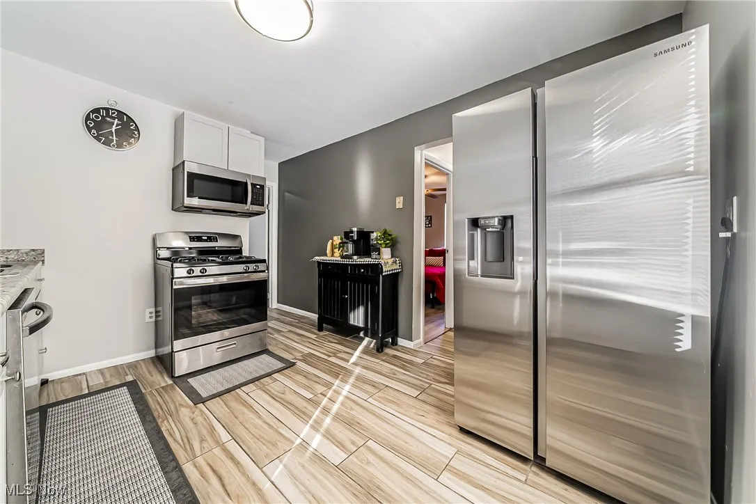 Kitchen with white cabinetry, wood tiled floor, appliances with stainless steel finishes, and baseboards