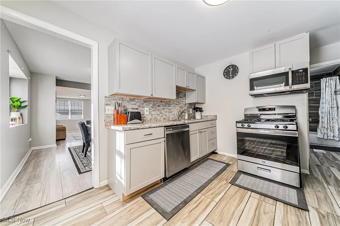 Kitchen with appliances with stainless steel finishes, a sink, light wood finished floors, and tasteful backsplash