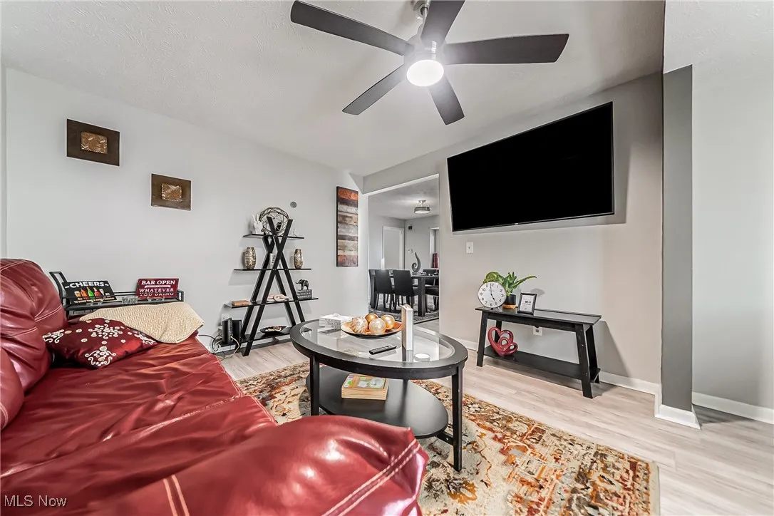 Living area with baseboards, ceiling fan, a textured ceiling, and light wood-style floors
