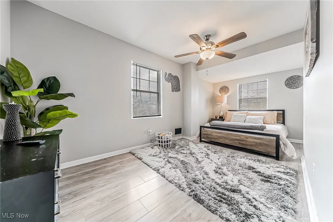 Bedroom with ceiling fan, multiple windows, wood finished floors, and baseboards