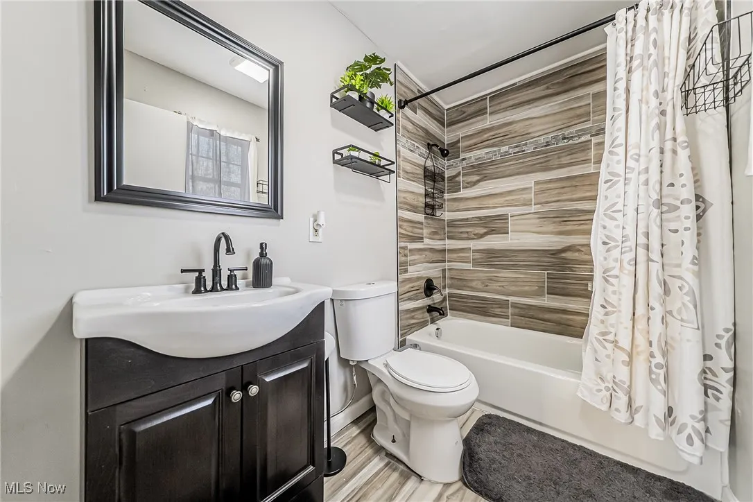 Full bath with toilet, shower / bath combo, wood finished floors, and vanity