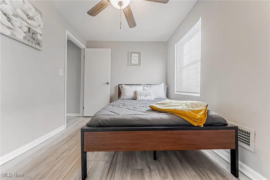 Bedroom with ceiling fan, light wood-style floors, visible vents, and baseboards