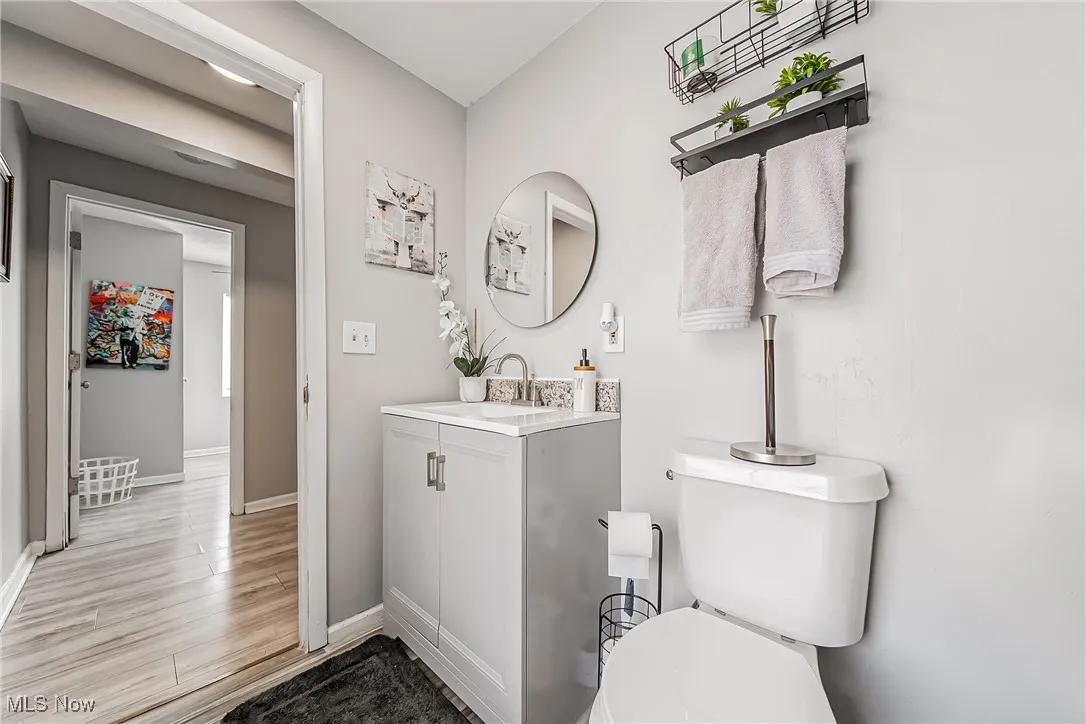 Half bathroom with vanity, wood finished floors, toilet, and baseboards