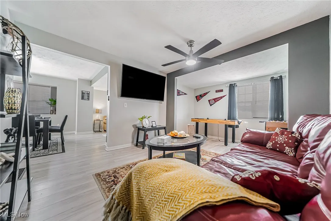 Living area featuring a ceiling fan, baseboards, light wood-style flooring, and a textured ceiling