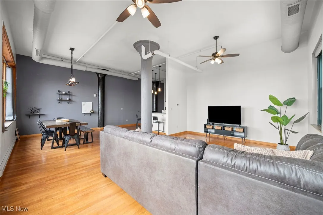 Living room featuring baseboards, visible vents, ceiling fan, and light wood finished floors