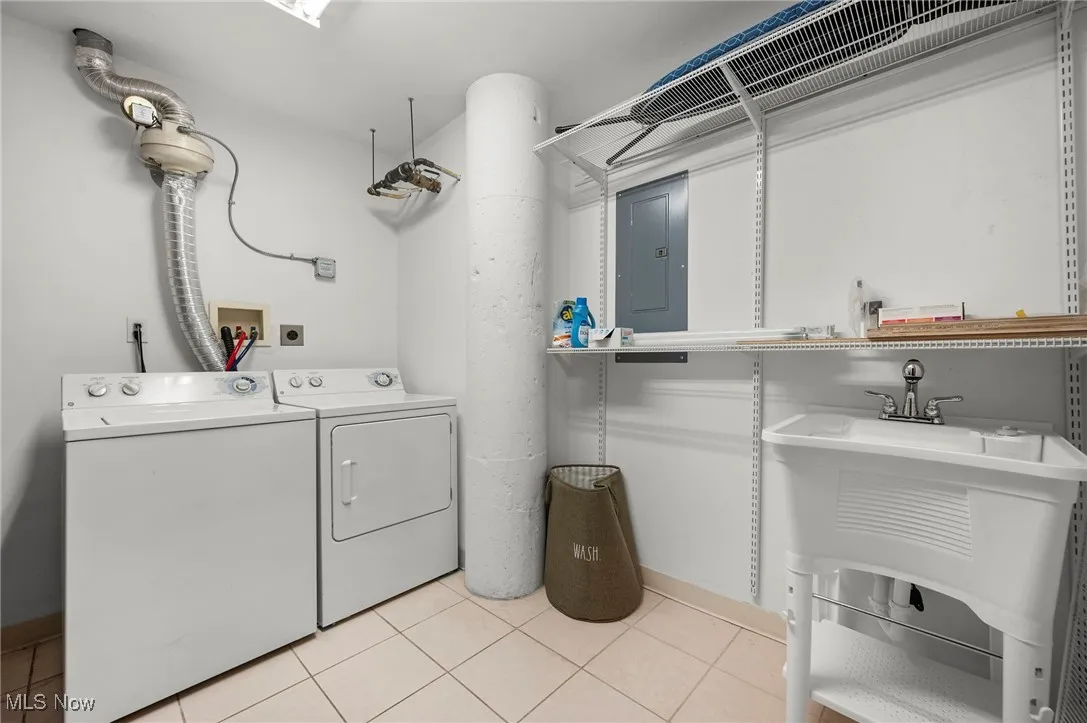 Clothes washing area with laundry area, washing machine and dryer, electric panel, and light tile patterned flooring