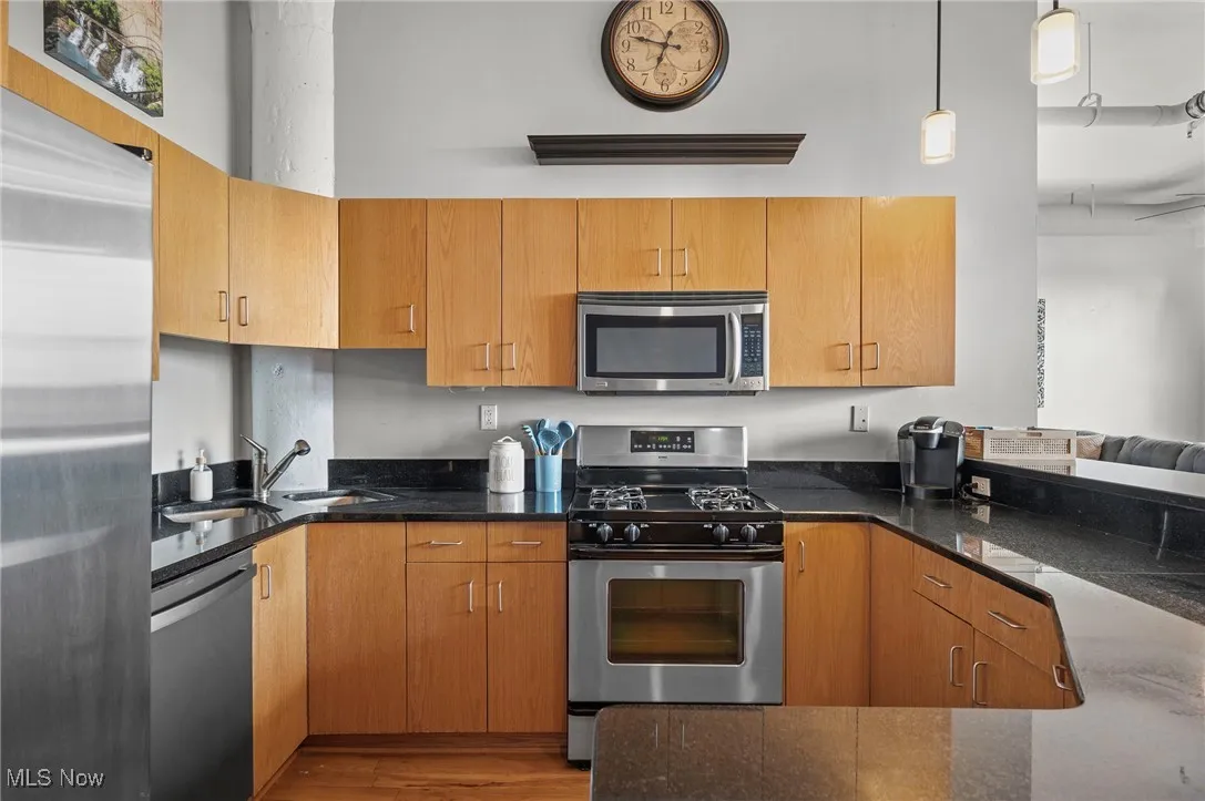 Kitchen featuring stainless steel appliances, decorative light fixtures, a sink, and dark stone countertops
