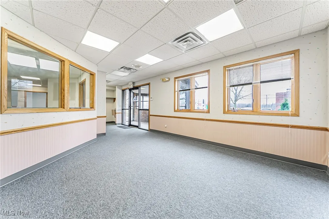 Empty room with a drop ceiling, wainscoting, and a healthy amount of sunlight