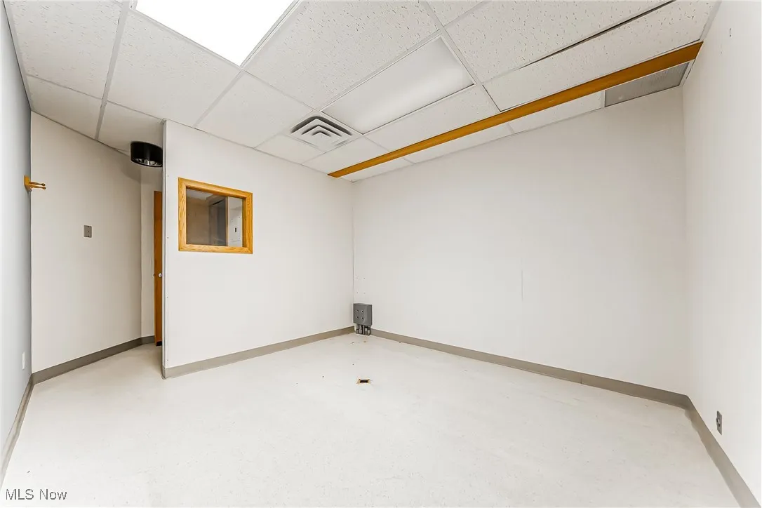 Empty room with a paneled ceiling, visible vents, and baseboards