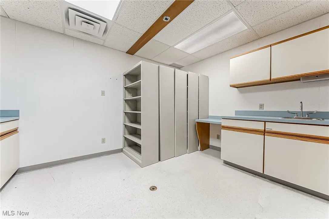 Kitchen featuring baseboards, a drop ceiling, and a sink