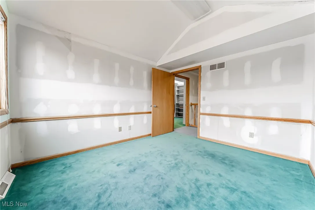 Spare room featuring carpet, visible vents, vaulted ceiling, and baseboards