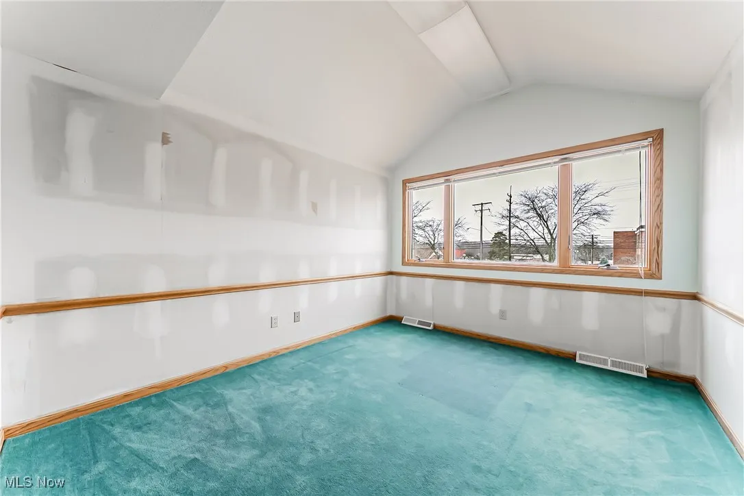 Carpeted empty room featuring lofted ceiling, visible vents, and baseboards