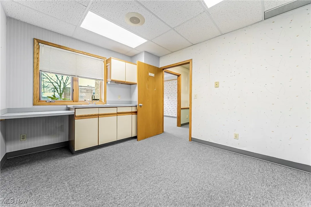 Kitchen featuring a paneled ceiling, light colored carpet, a sink, baseboards, and light countertops