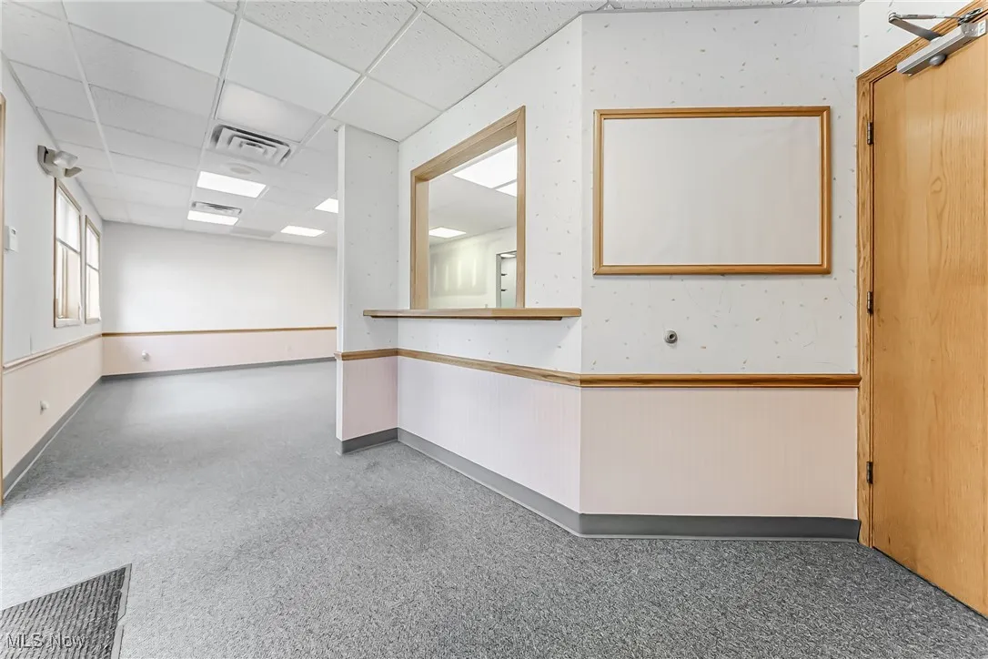 Empty room featuring a wainscoted wall, a drop ceiling, and visible vents