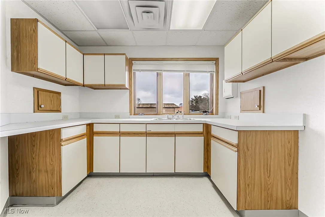 Kitchen featuring light countertops, a sink, a paneled ceiling, and white cabinets