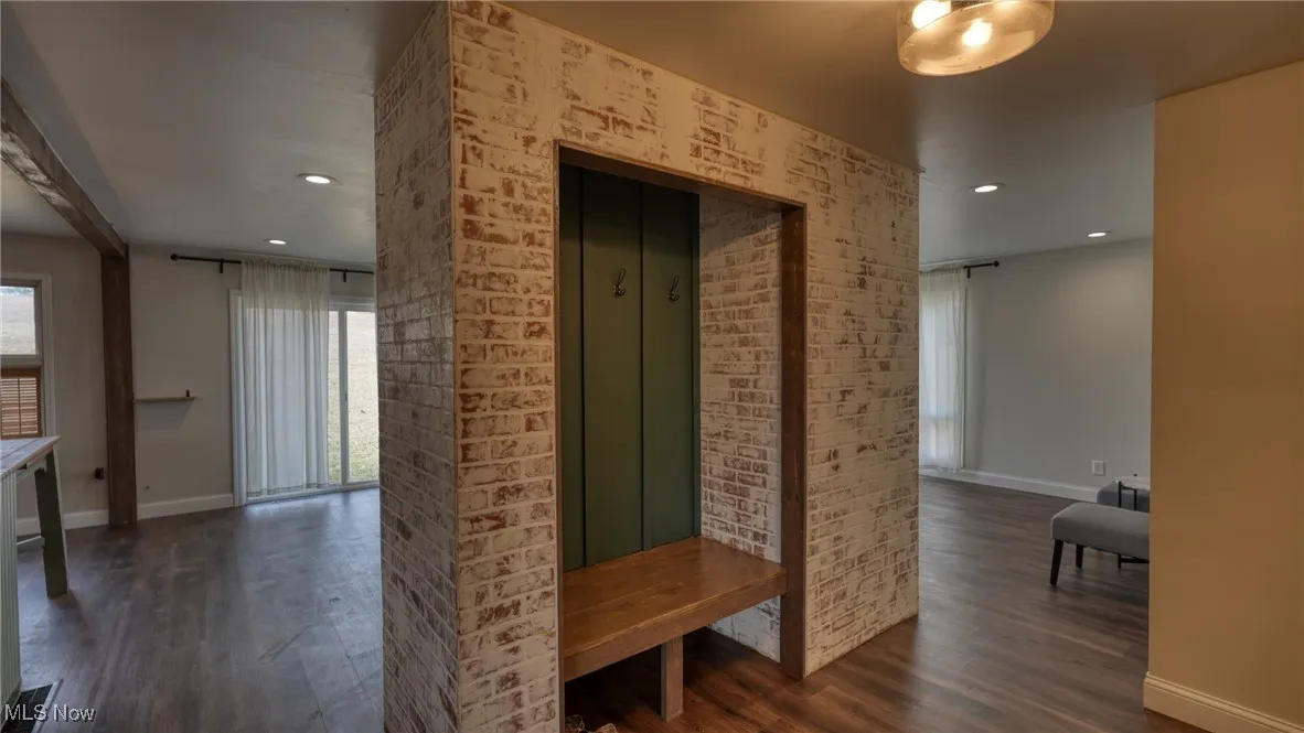 Hallway featuring recessed lighting, dark wood-style flooring, brick wall, and baseboards