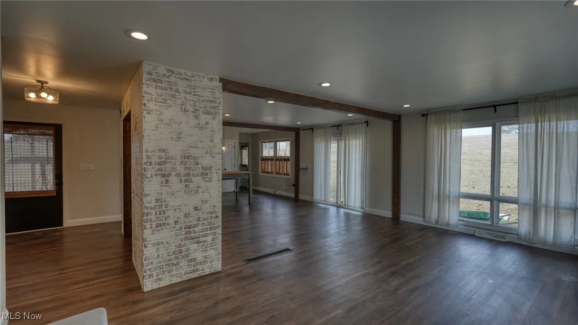 Unfurnished living room with dark wood-type flooring, a wealth of natural light, visible vents, and baseboards