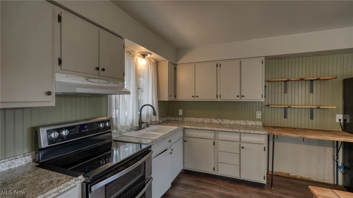 Kitchen featuring range with two ovens, light countertops, dark wood-type flooring, a sink, and under cabinet range hood