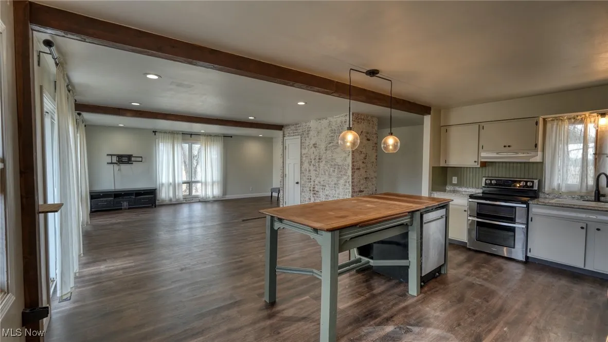 Kitchen with under cabinet range hood, beam ceiling, double oven range, dark wood finished floors, and pendant lighting