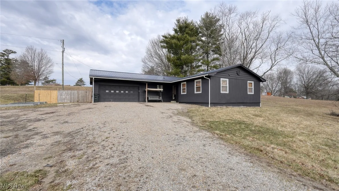 Ranch-style home featuring metal roof, a garage, fence, driveway, and a front lawn