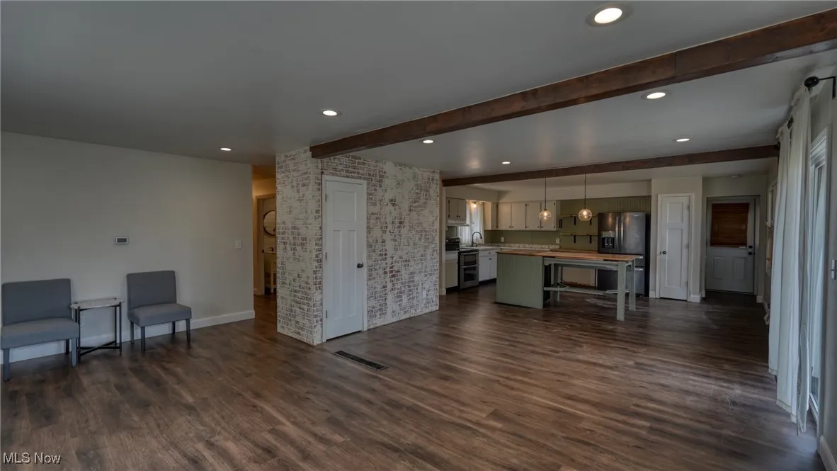 Living room featuring dark wood finished floors, recessed lighting, visible vents, brick wall, and beamed ceiling