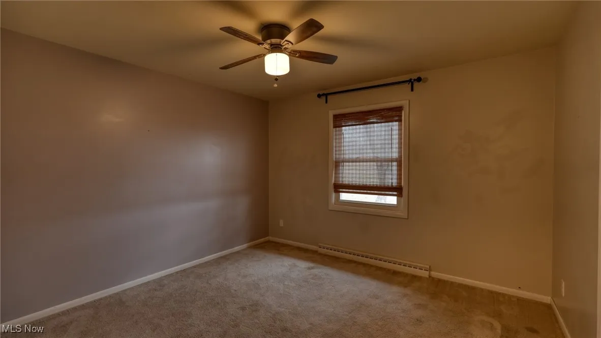 Empty room with a ceiling fan, a baseboard radiator, carpet flooring, and baseboards