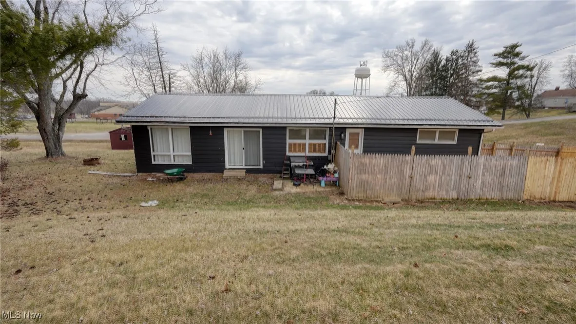 View of front of property featuring metal roof, fence, and a front lawn
