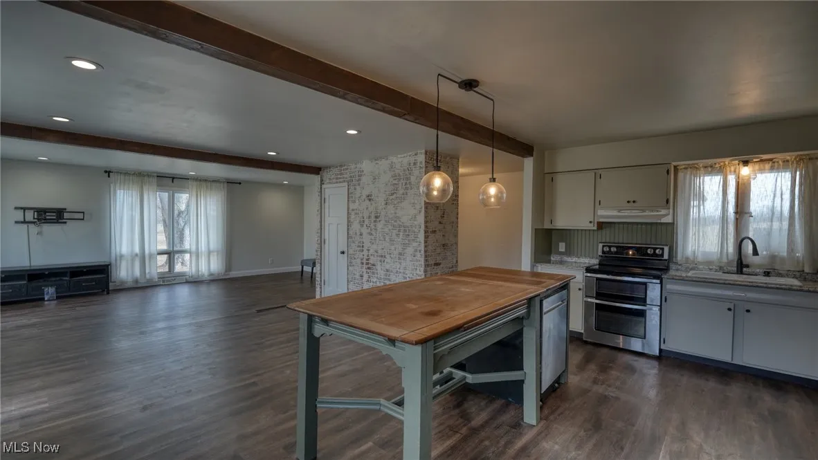 Kitchen with range with two ovens, under cabinet range hood, dark wood-type flooring, a sink, and beam ceiling
