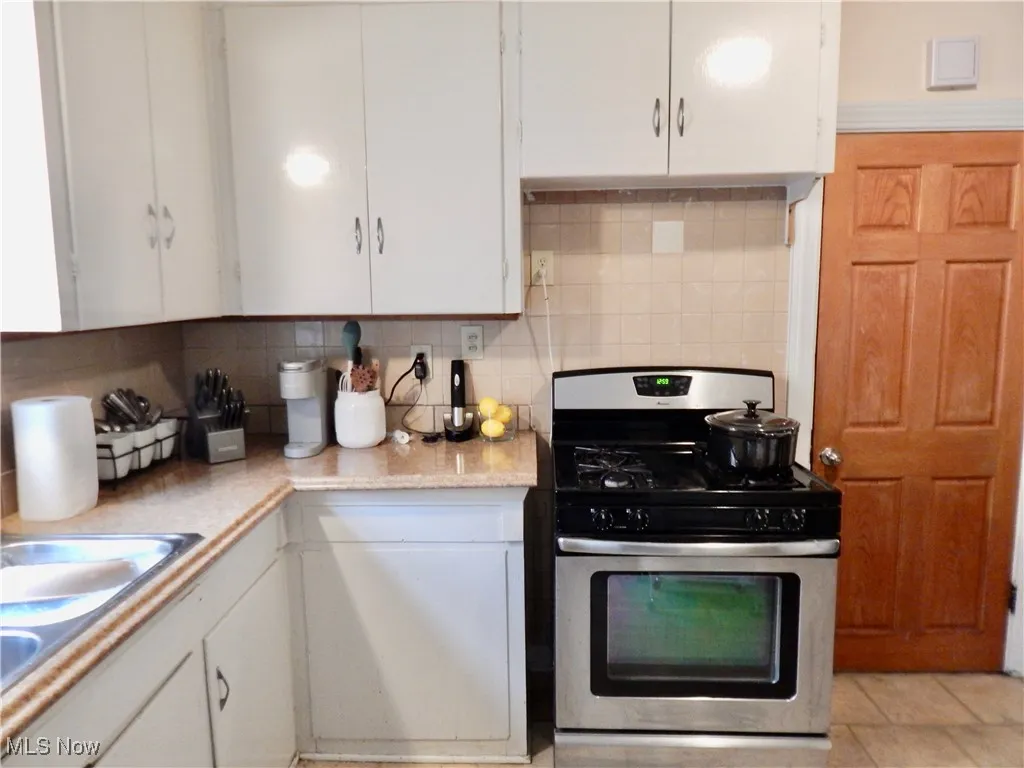 Kitchen featuring stainless steel gas range oven, white cabinetry, and backsplash