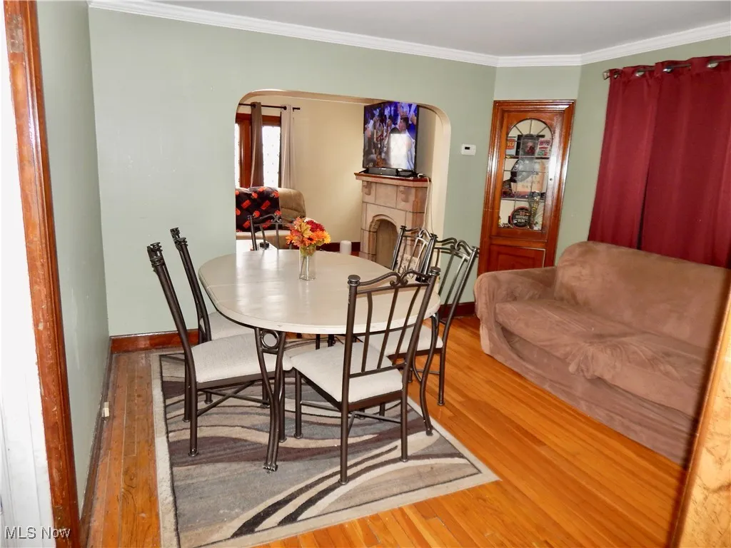 Dining area featuring arched walkways, hardwood floors, baseboards, ornamental molding, and a tiled fireplace