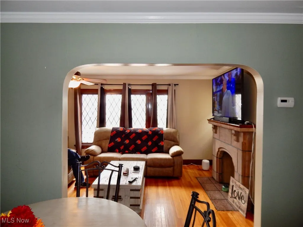 Living area featuring ornamental molding, arched walkways, a fireplace with flush hearth, and hardwood  floors