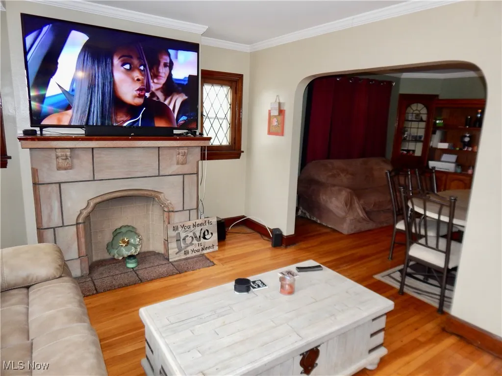 Living room featuring arched walkways, a tiled fireplace, ornamental molding, hardwood floors, and baseboards