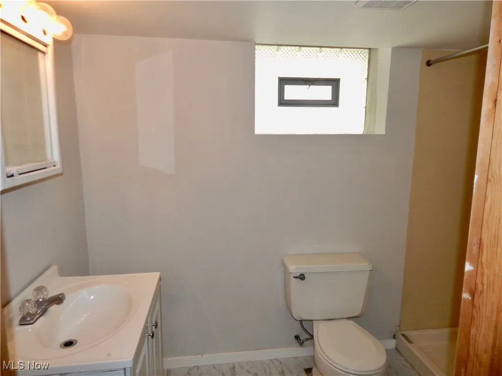 Basement Full bath with toilet, a shower, vanity, and baseboards