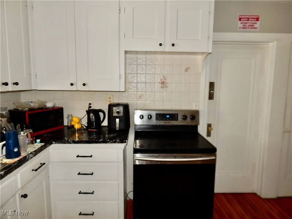 Upstairs unit Kitchen featuring white cabinets, backsplash, and range with electric stovetop