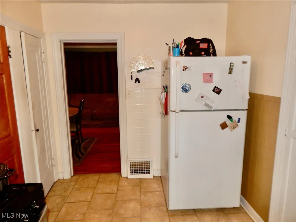 Kitchen featuring light tile patterned floors, wainscoting, refrigerator, and tile walls