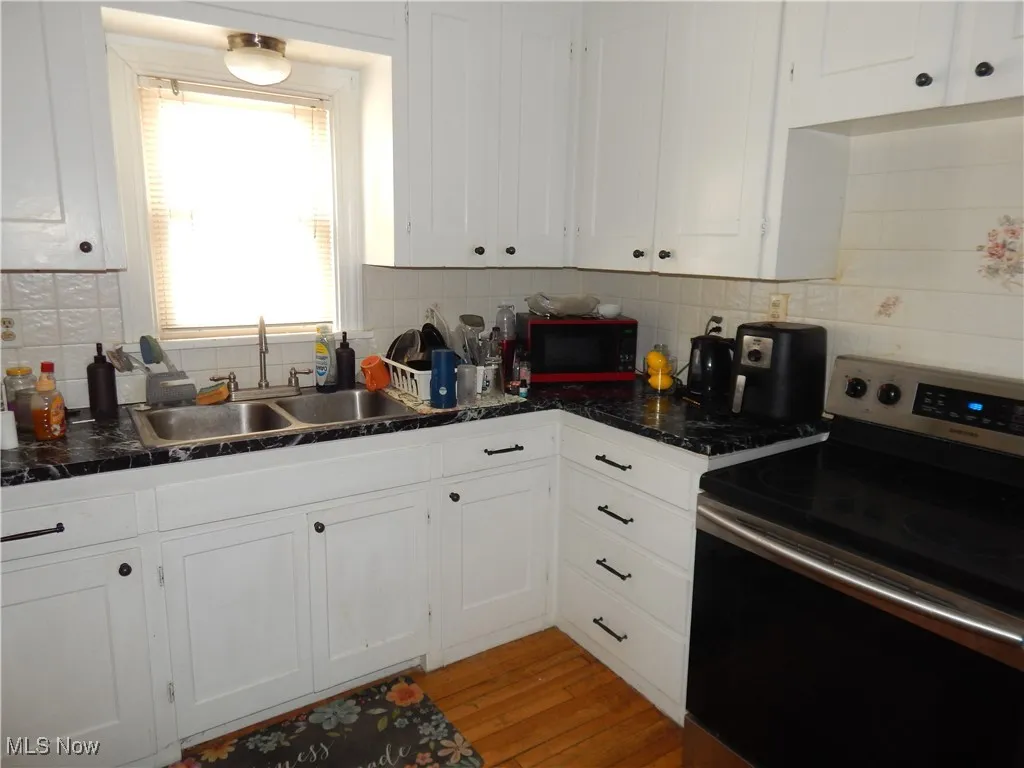 Upstairs unit Kitchen featuring stainless steel electric stove, hardwood floors, white cabinetry, a sink, and black microwave