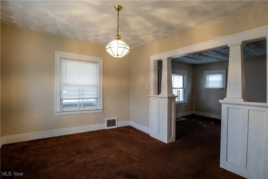 Dining area with ornate columns, baseboards, and dark carpet
