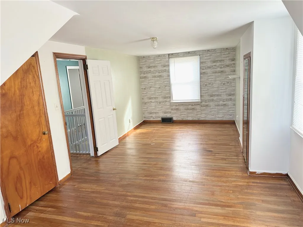 Additional living space featuring brick wall, visible vents, baseboards, and wood finished floors