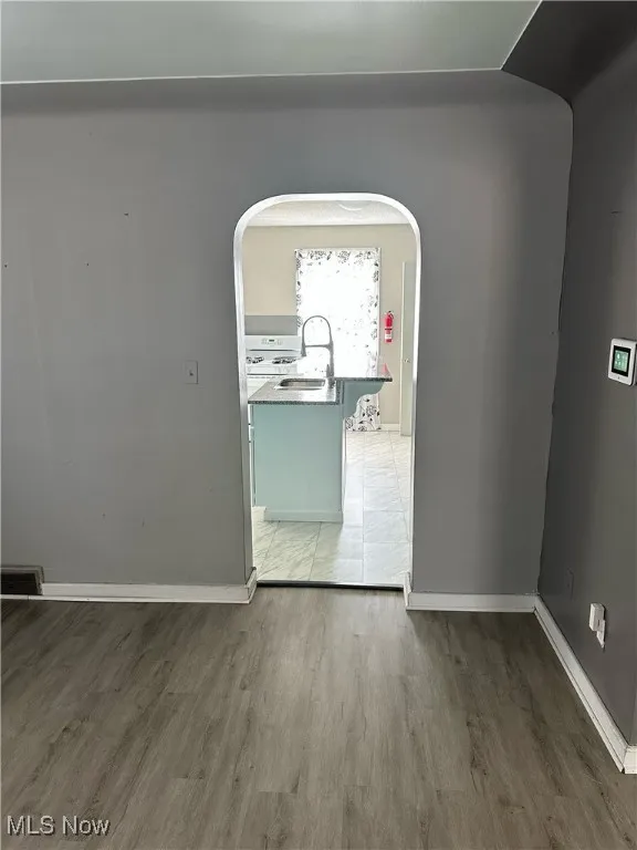 Empty room featuring arched walkways, light wood-style flooring, a sink, visible vents, and baseboards