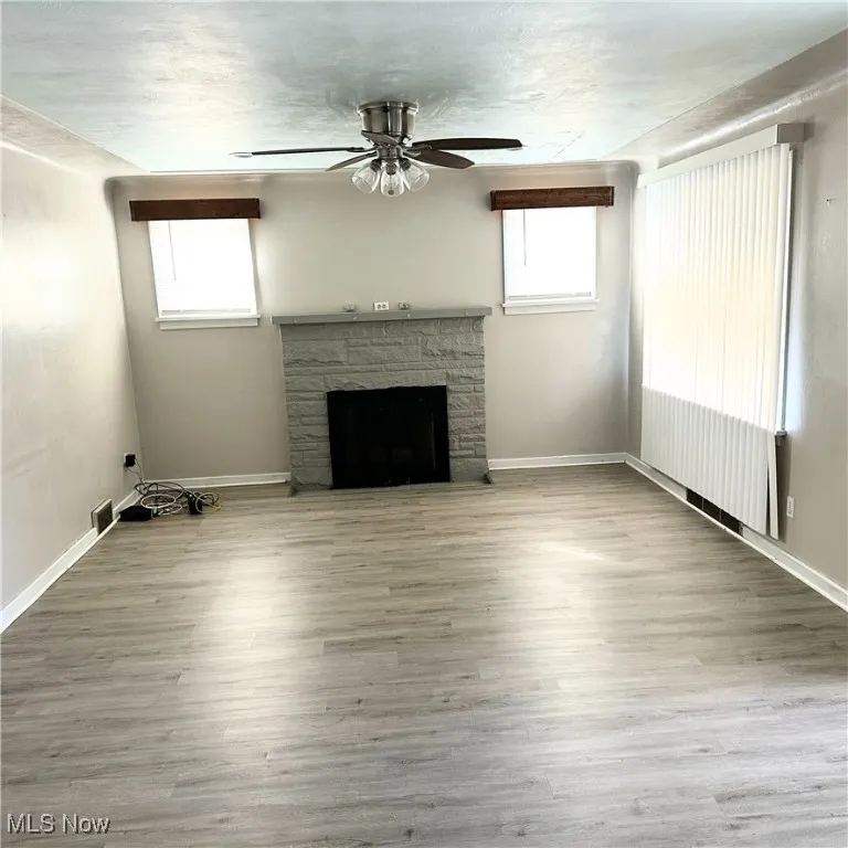 Unfurnished living room with a wealth of natural light, baseboards, wood finished floors, and a stone fireplace