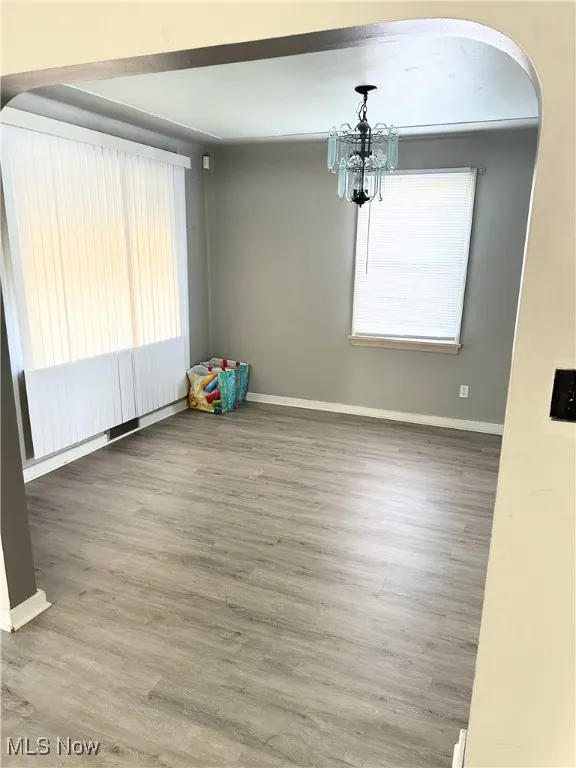 Unfurnished room featuring a notable chandelier, baseboards, arched walkways, and wood finished floors