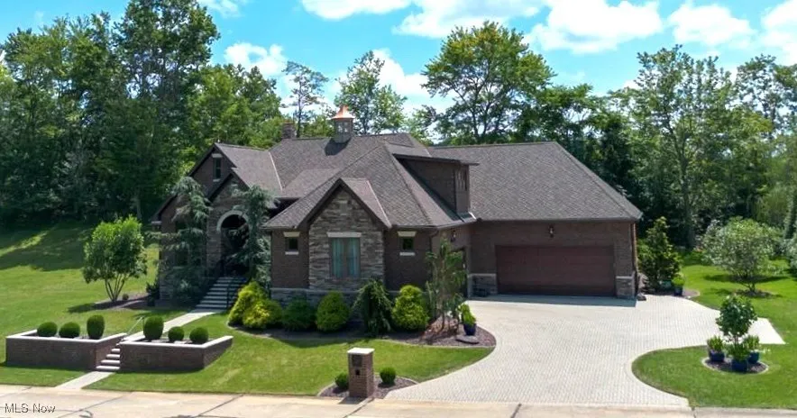 Craftsman inspired home featuring stone siding, a front lawn, decorative driveway, a garage, and view of scattered trees