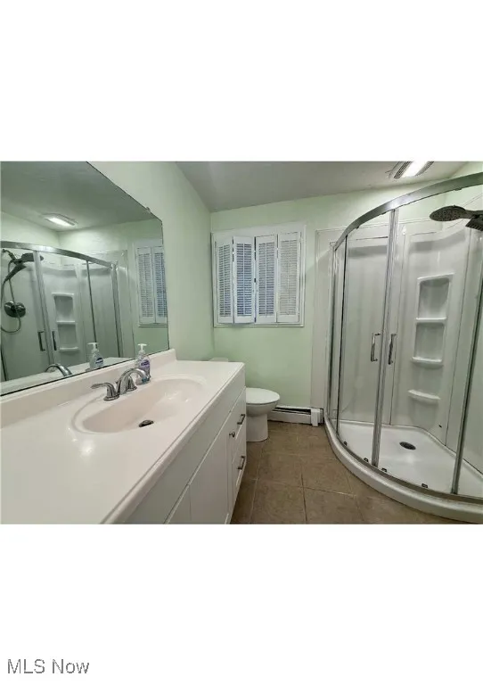 Bathroom featuring a stall shower, vanity, dark tile patterned floors, and a baseboard heating unit