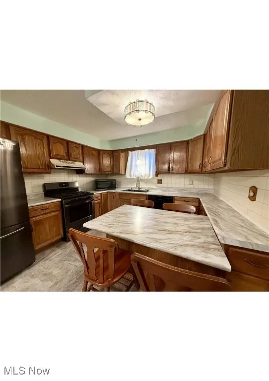 Kitchen featuring light countertops, black appliances, brown cabinets, tasteful backsplash, and a breakfast bar