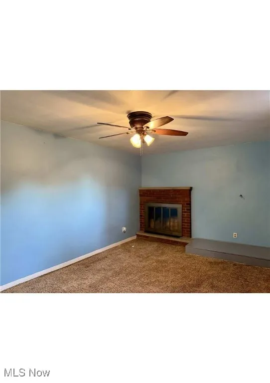 Carpeted spare room with a fireplace and ceiling fan