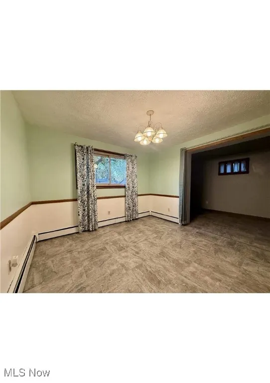 Spare room featuring a baseboard heating unit, a textured ceiling, and a chandelier